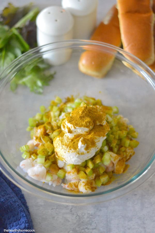 Chopped shrimp and celery in a large glass bowl. Topped with Greek yogurt and curry seasoning.