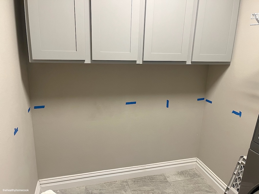 Image of black wall with blue tape. Measuring out where cabinets need to be placed.
