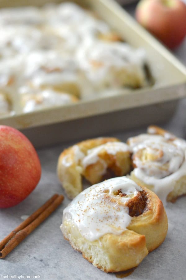 Profile image of Apple Cinnamon Rolls. One cinnamon roll close up, remaining rolls in pan behind.